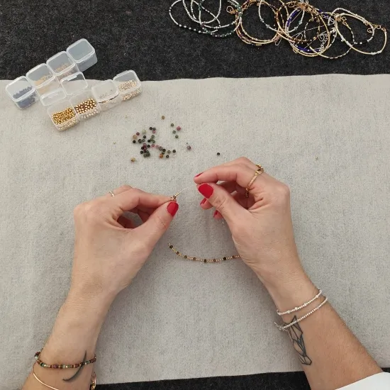 Mains qui enfilent des perles d’or sur un fil, à l’établi