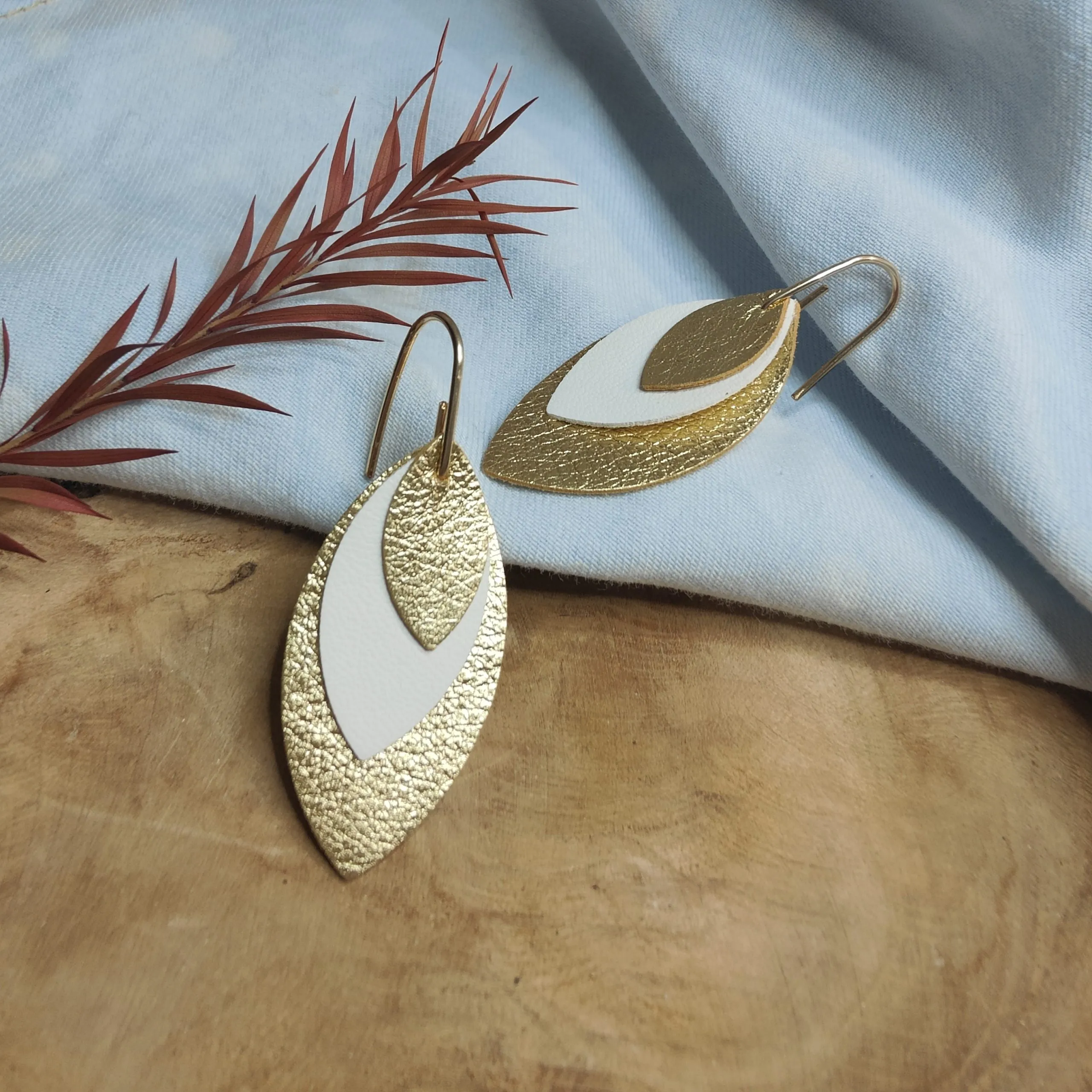 Boucles d’oreilles feuilles dorées posées sur du bois flotté