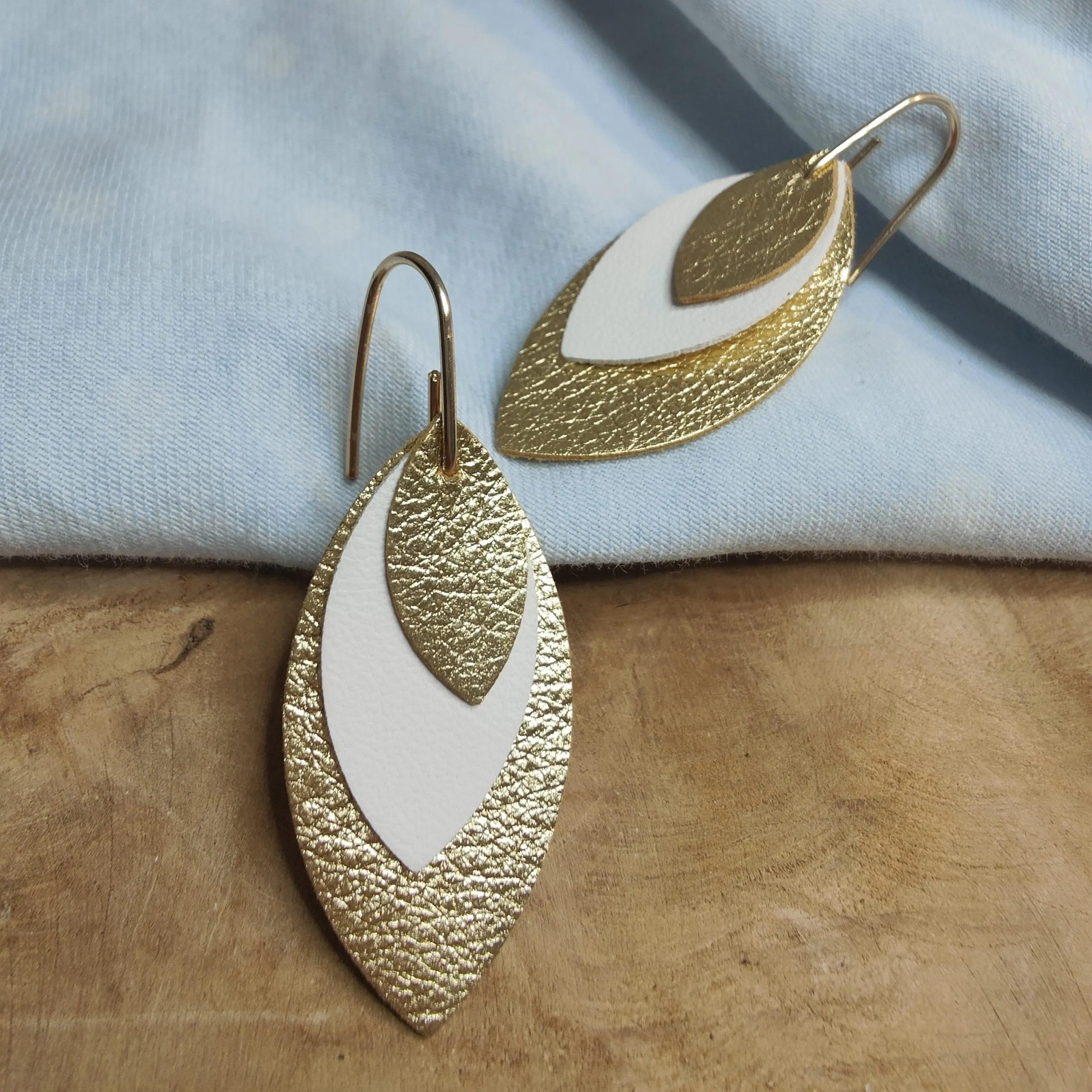Boucles d’oreilles feuilles en cuir doré et blanc sur un plateau de bois